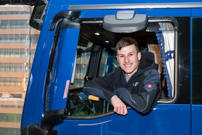 ein junger LKW-Kraftfahrer lächelt aus der Fahrerkabine eines LKWs der Firma EFT